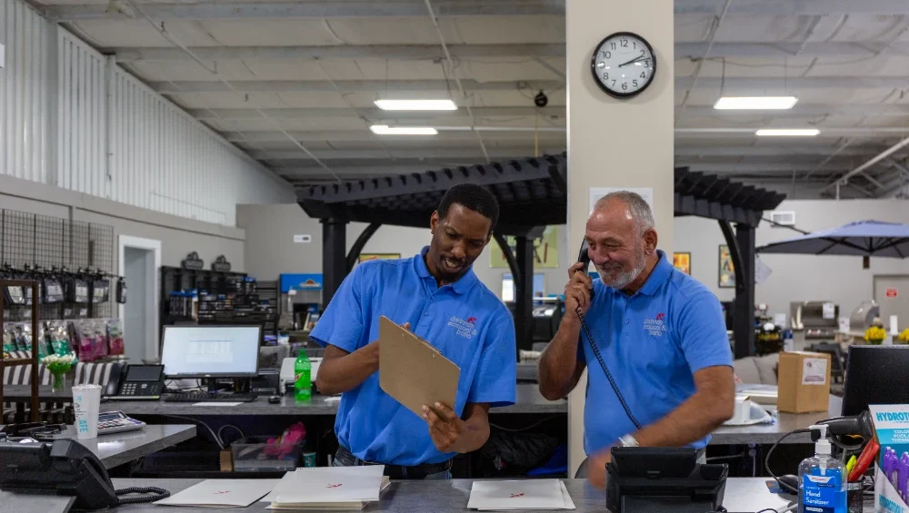 Two Cincinnati pools and patio employees in blue shirts discuss pool supplies at customer service desk