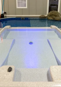 Modern hot tub with blue LED lighting next to indoor swimming pool