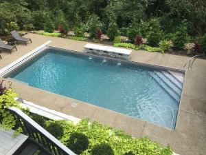 Modern backyard pool with concrete patio, lounge chairs, and landscaping