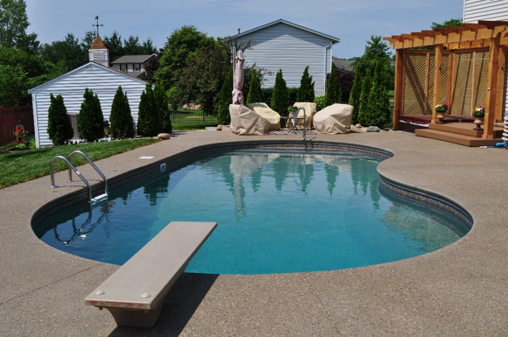Luxury backyard pool with diving board, patio furniture, and wooden pergola in Cincinnati outdoor living space