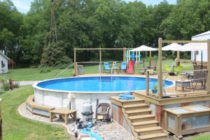 Above ground pool with wooden deck, patio furniture, and landscaped backyard oasis