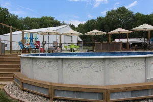 Above ground pool with wooden deck, patio umbrellas, and outdoor furniture in backyard