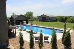 Luxury backyard pool with lounge chairs, umbrellas, and outdoor patio furniture surrounded by landscaping