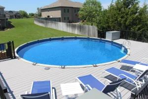 Above ground backyard pool with blue water and lounge chairs on composite deck