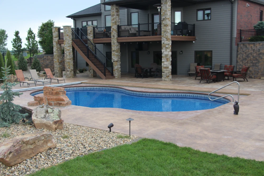 Luxury backyard pool with stone patio, outdoor furniture, and modern home installation