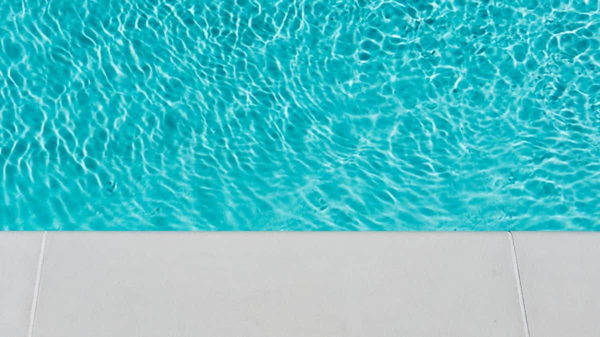 Clear blue swimming pool water at the edge of a concrete pool deck