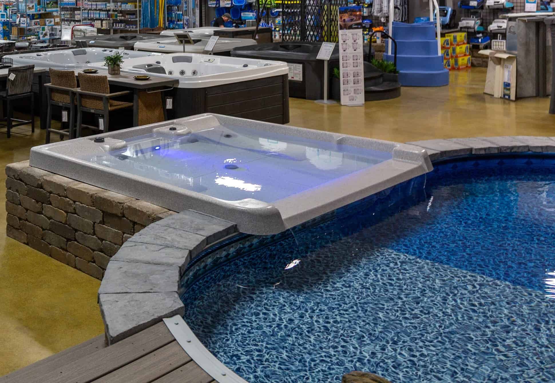 Spillover hot tub and inground display pool beside rows of hot tubs inside the Cincinnati Pool and Patio showroom on Reading Road